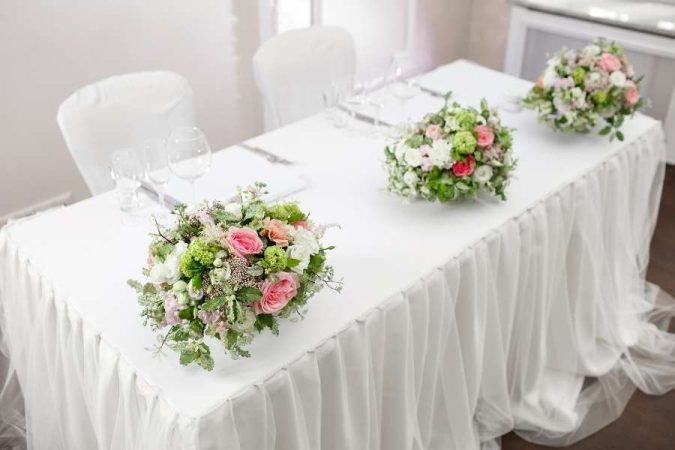 Une décoration de table de mariage élégante avec des nappes blanches drapées et des centres de table floraux roses et verts.