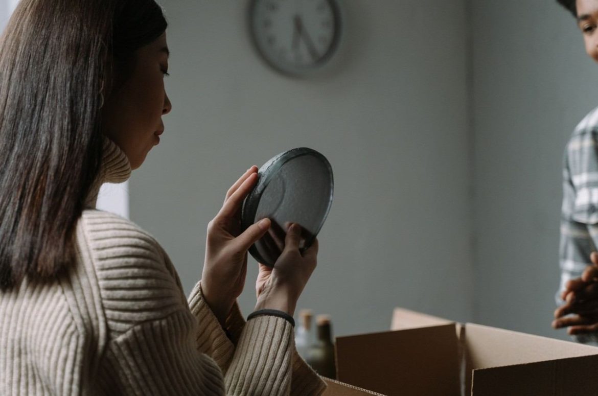 Une femme inspecte avec déception une assiette abîmée sortie d'un carton, illustrant le recours en cas d'objets cassés par les déménageurs professionnels.