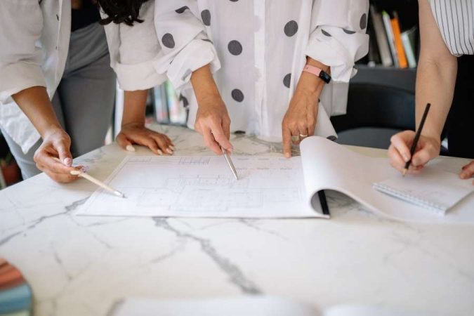Plusieurs personnes se penchent sur un plan de plomberie étalé sur une table.